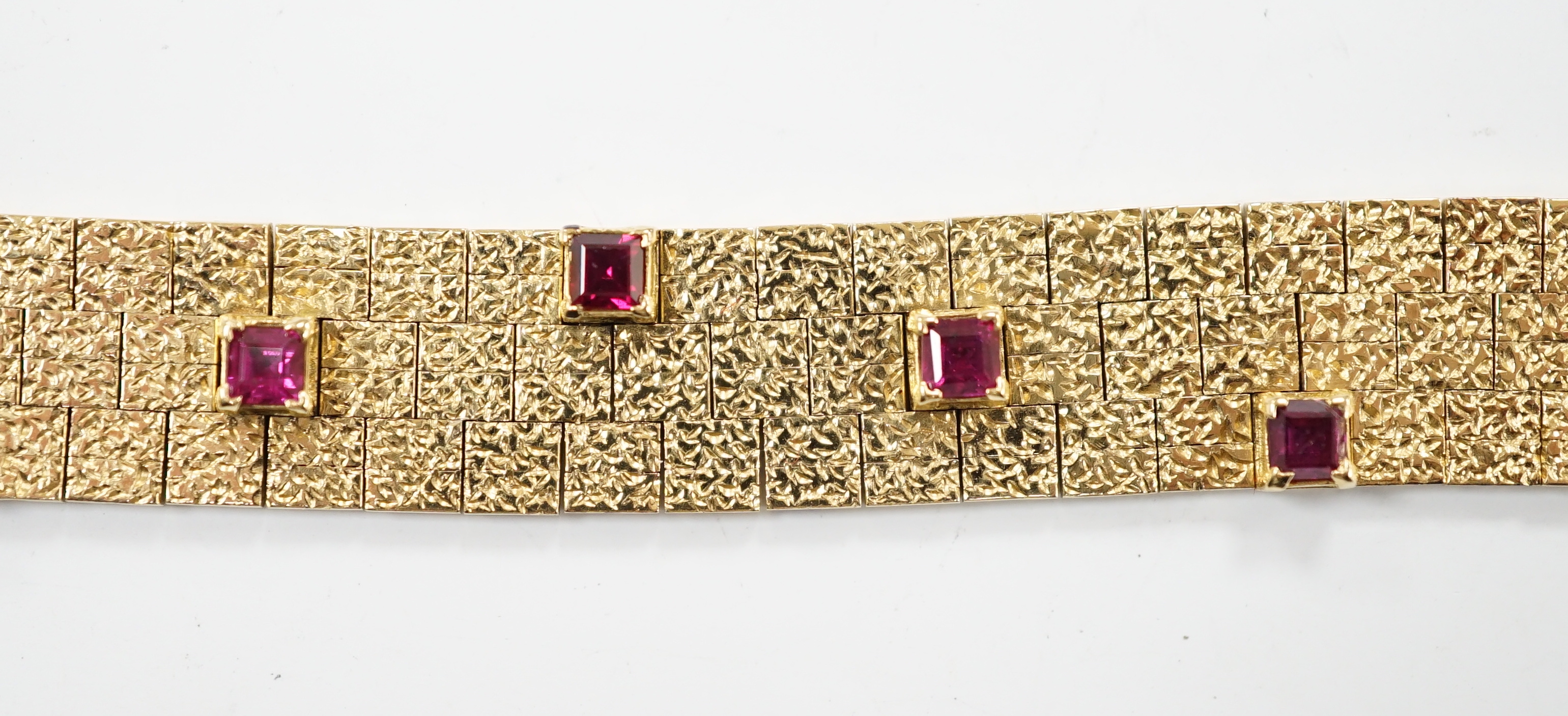 A textured yellow metal and eleven stone square cut ruby set bracelet, 16.5cm, gross weight 36.8 grams.